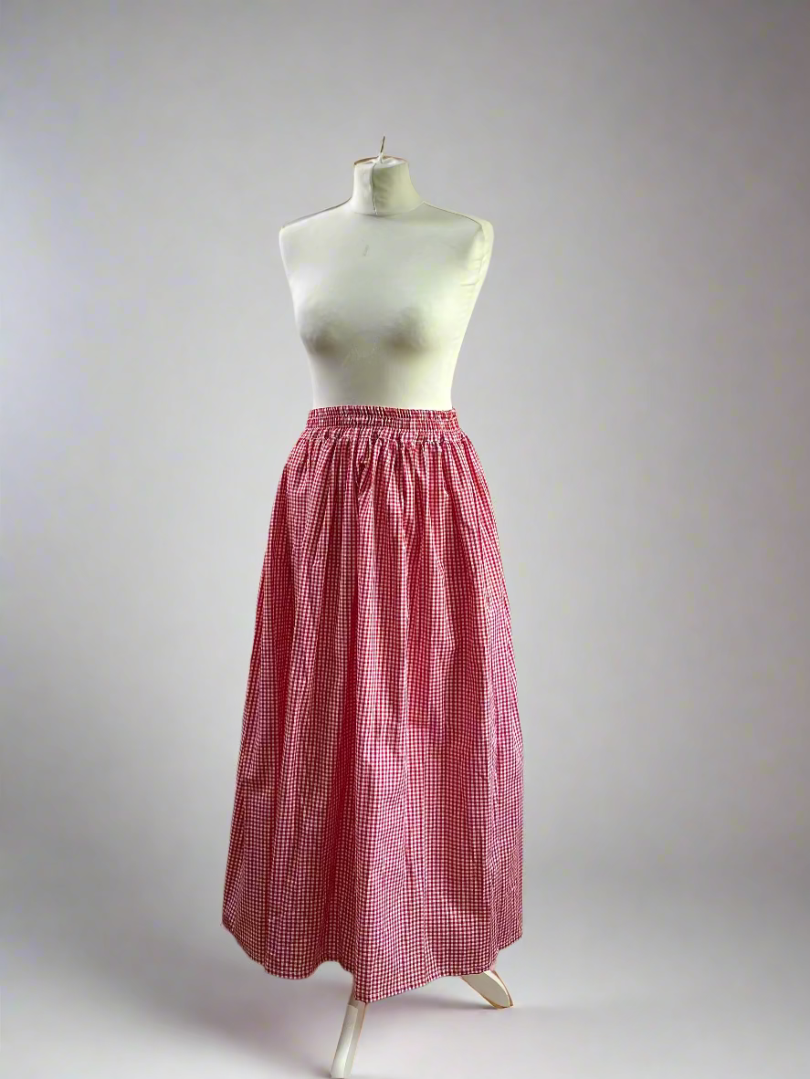 Mannequin wearing a red checkered skirt against a plain wall.