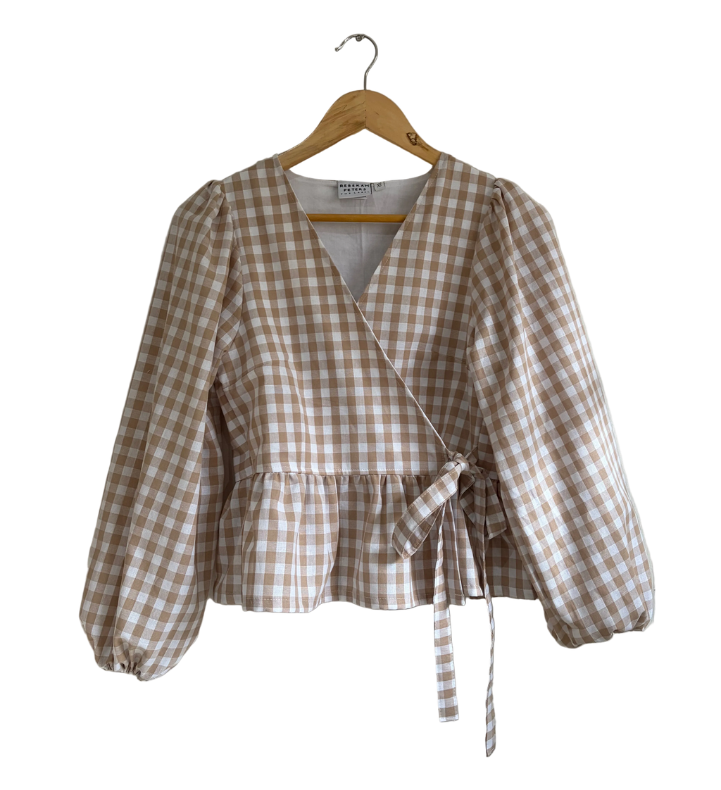 A beige and brown gingham wrap-style blouse with balloon sleeves, hanging on a wooden hanger against a plain white background.