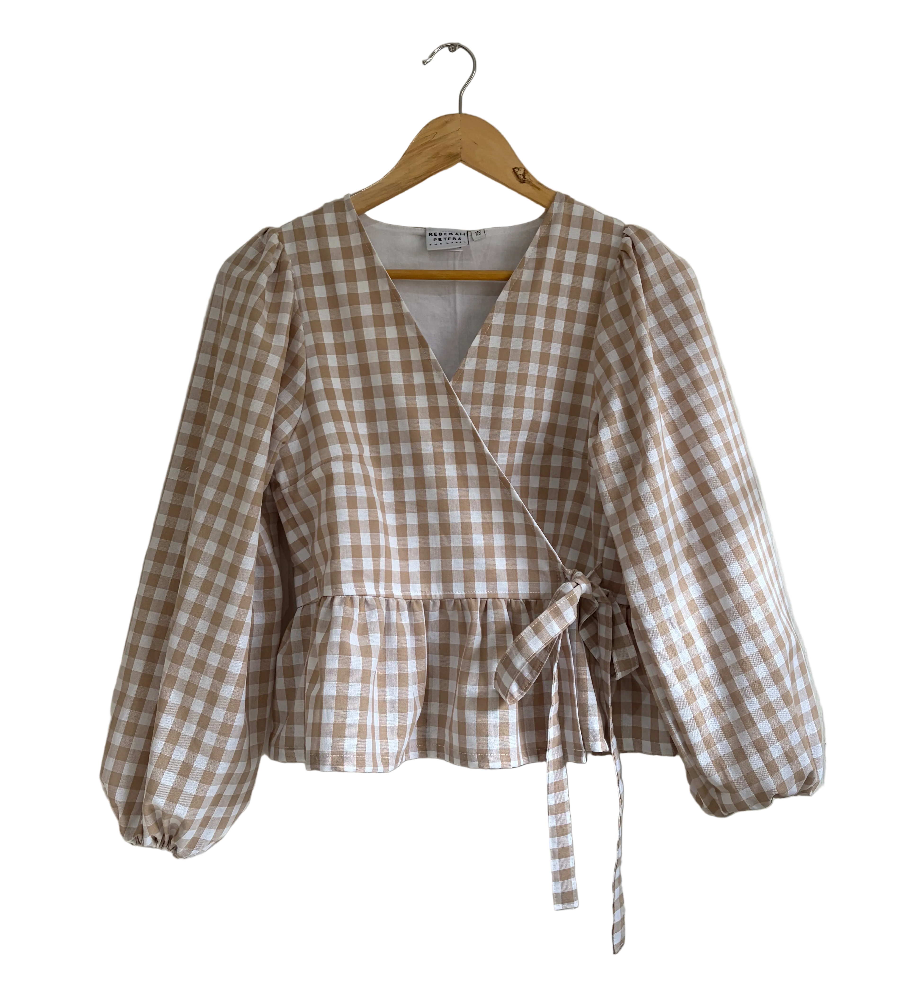 A beige and brown gingham wrap-style blouse with balloon sleeves, hanging on a wooden hanger against a plain white background.