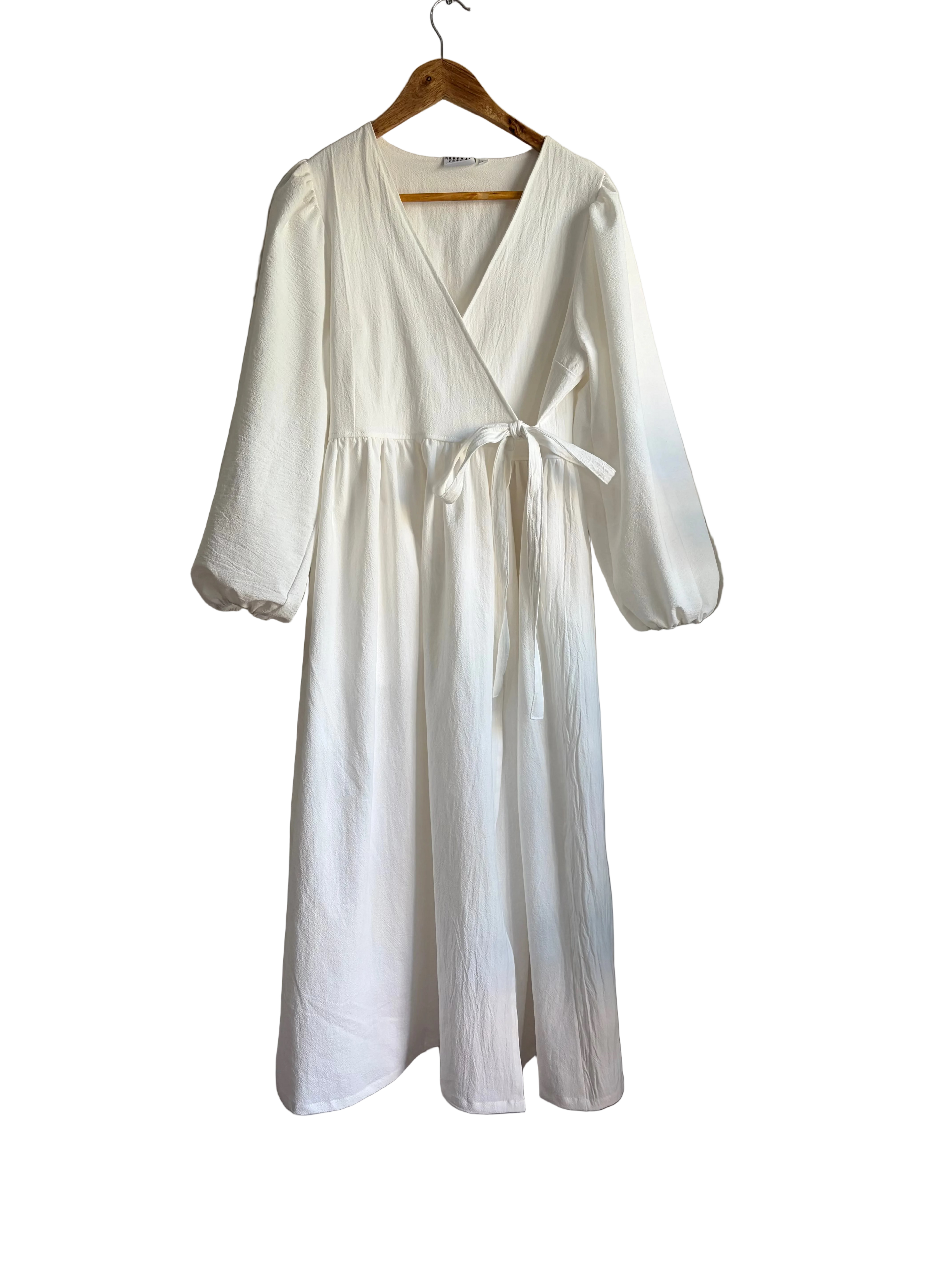 A white long-sleeve wrap dress with a tie waist, hanging on a wooden hanger/.