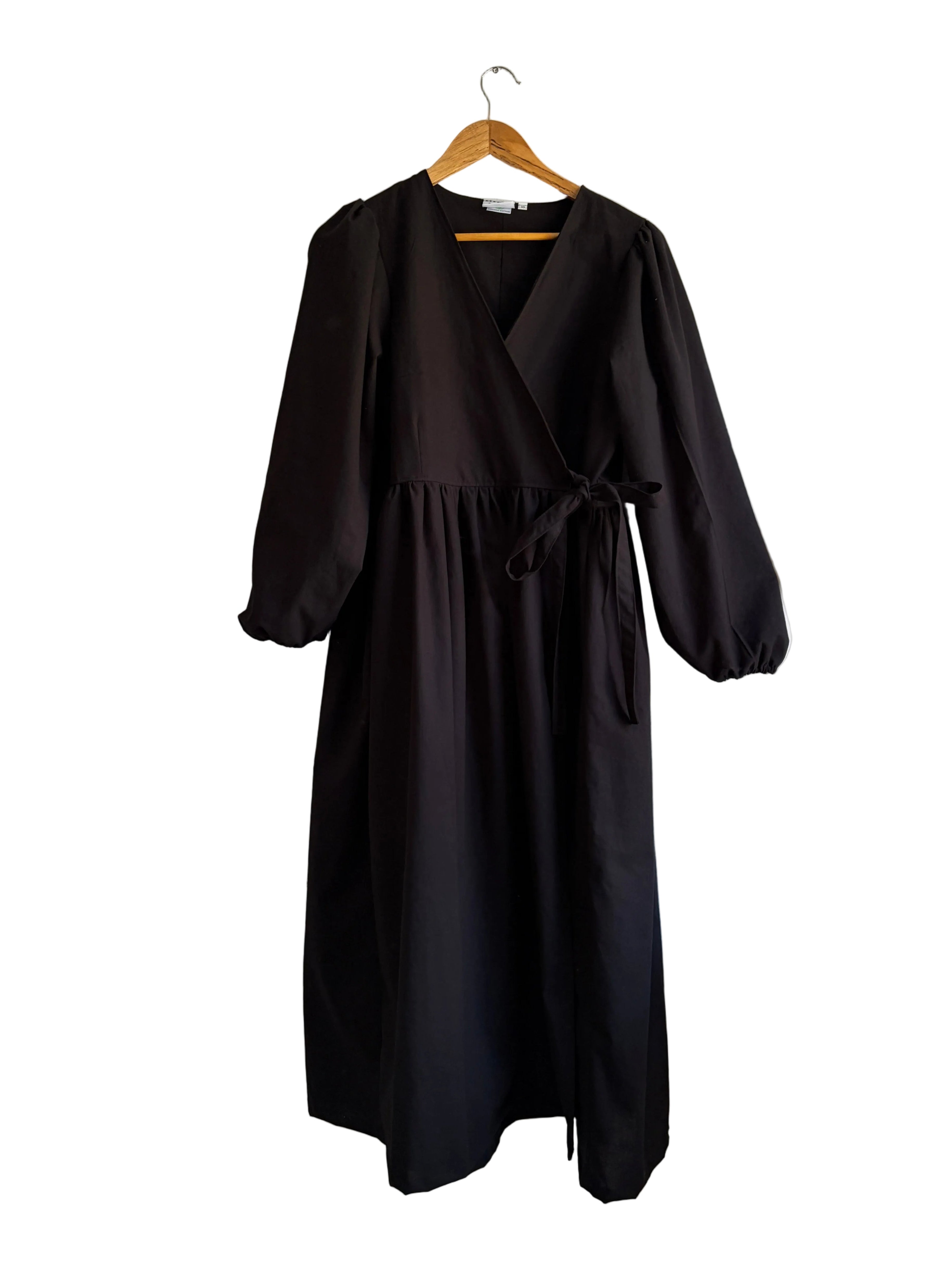 Black cotton wrap dress on a hanger against a white wall