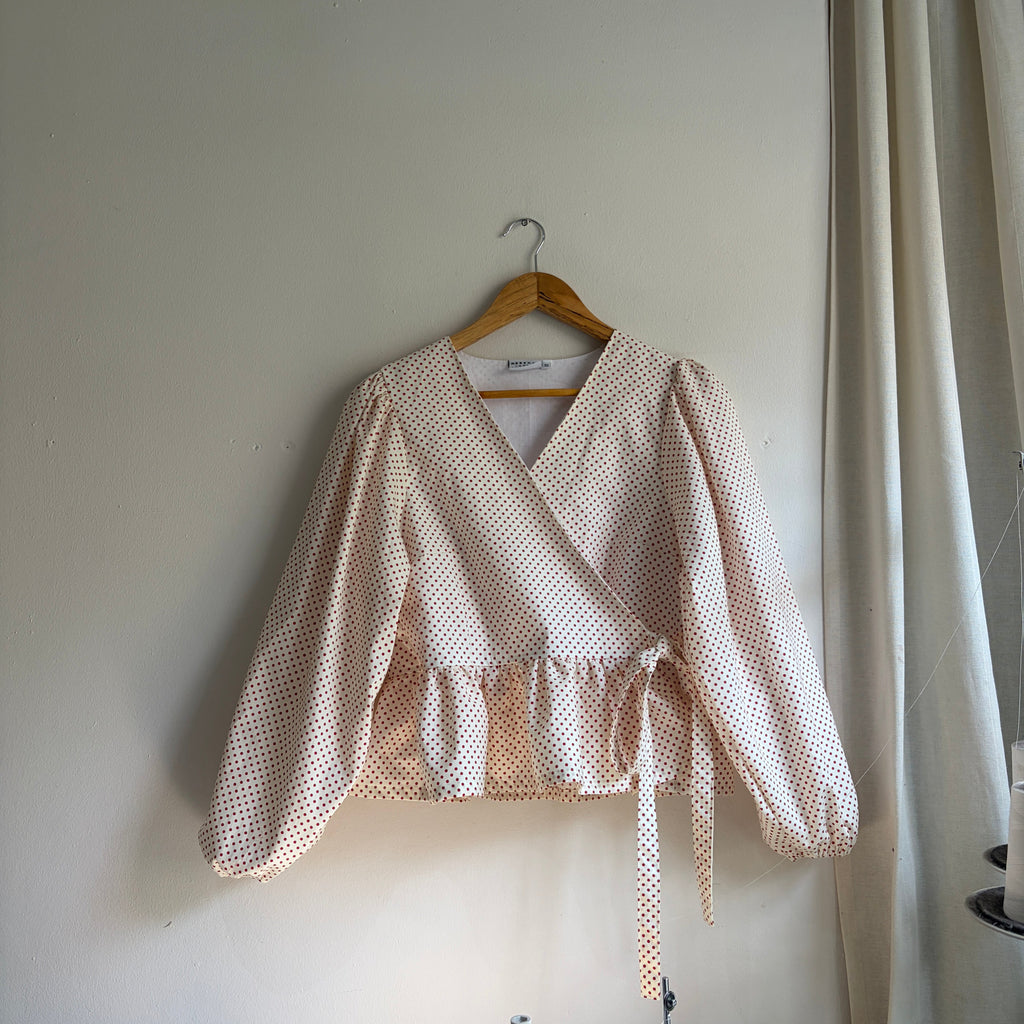 White blouse with ruffled details on a hanger against a white background