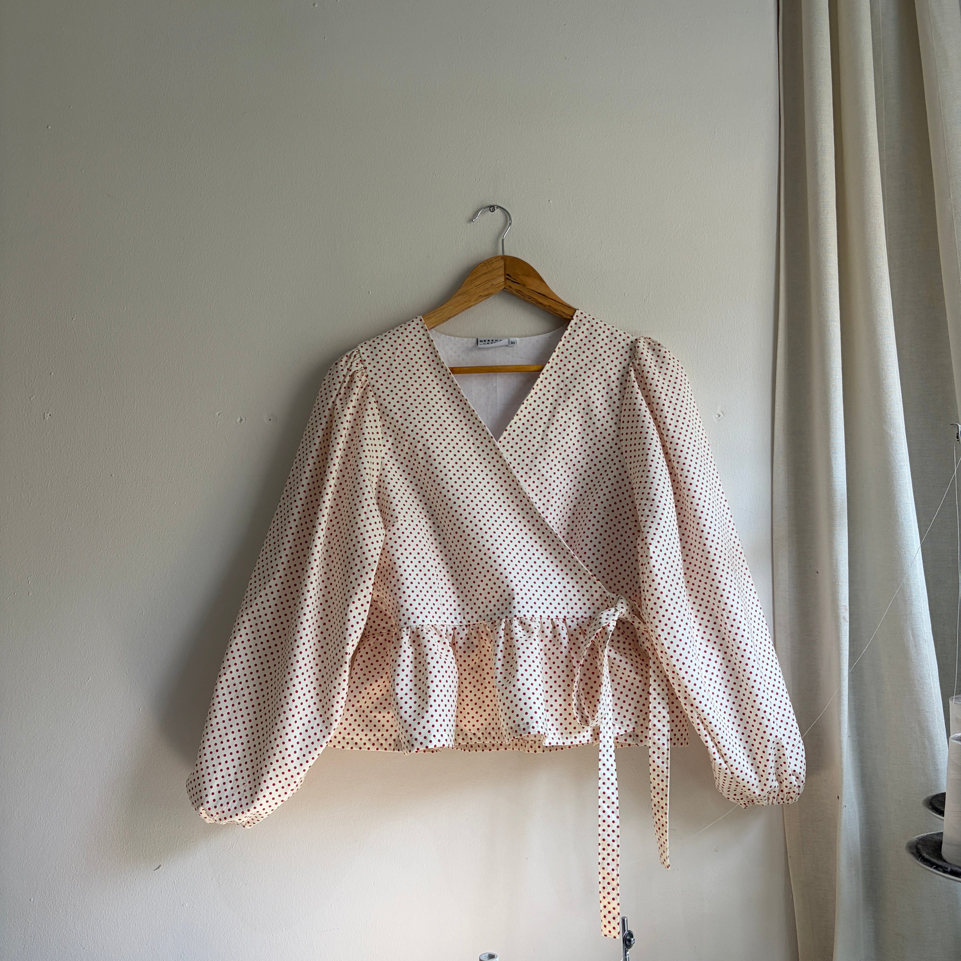 White blouse with ruffled details on a hanger against a white background