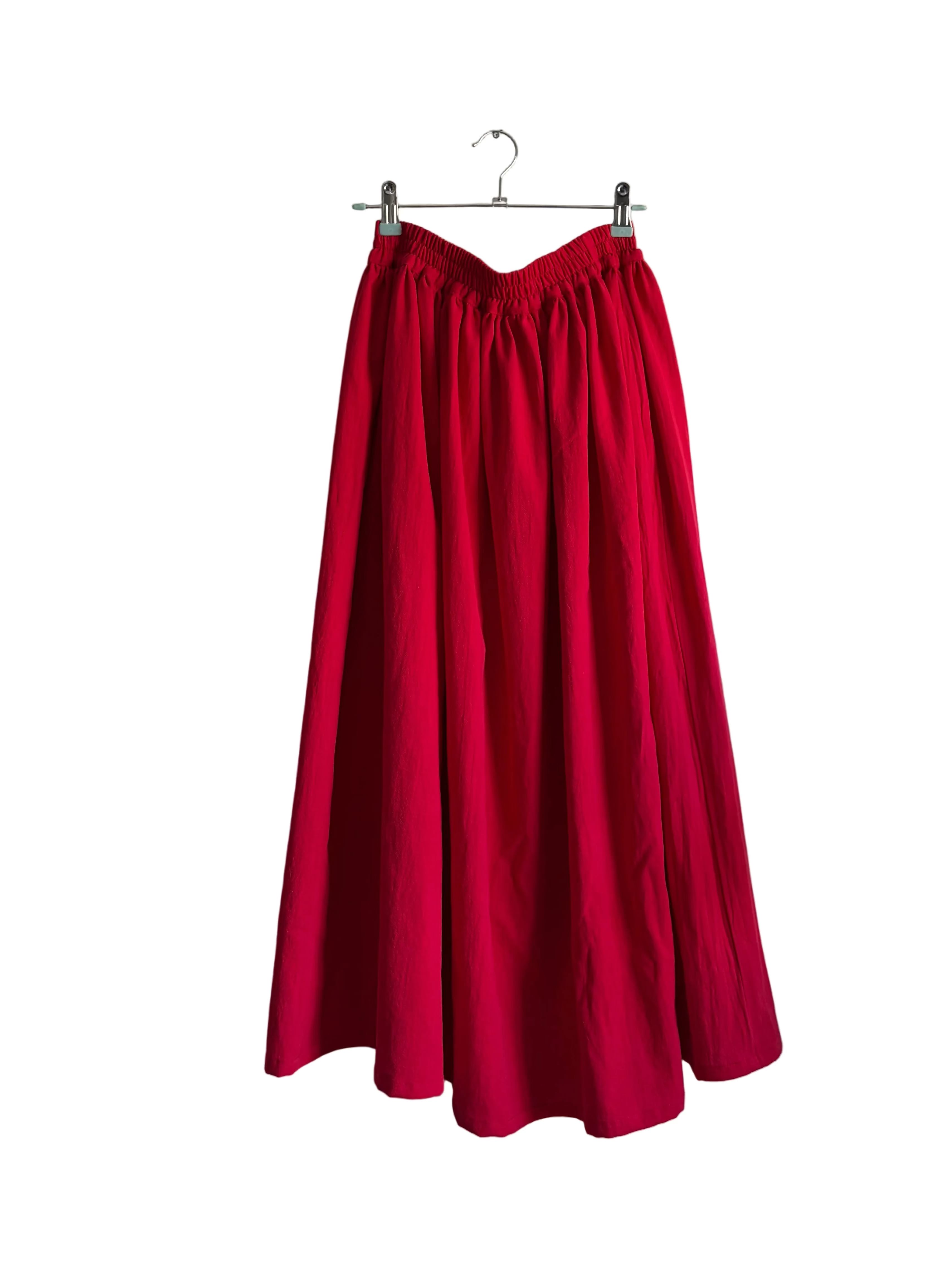 Red skirt hanging on a hanger against a white wall.
