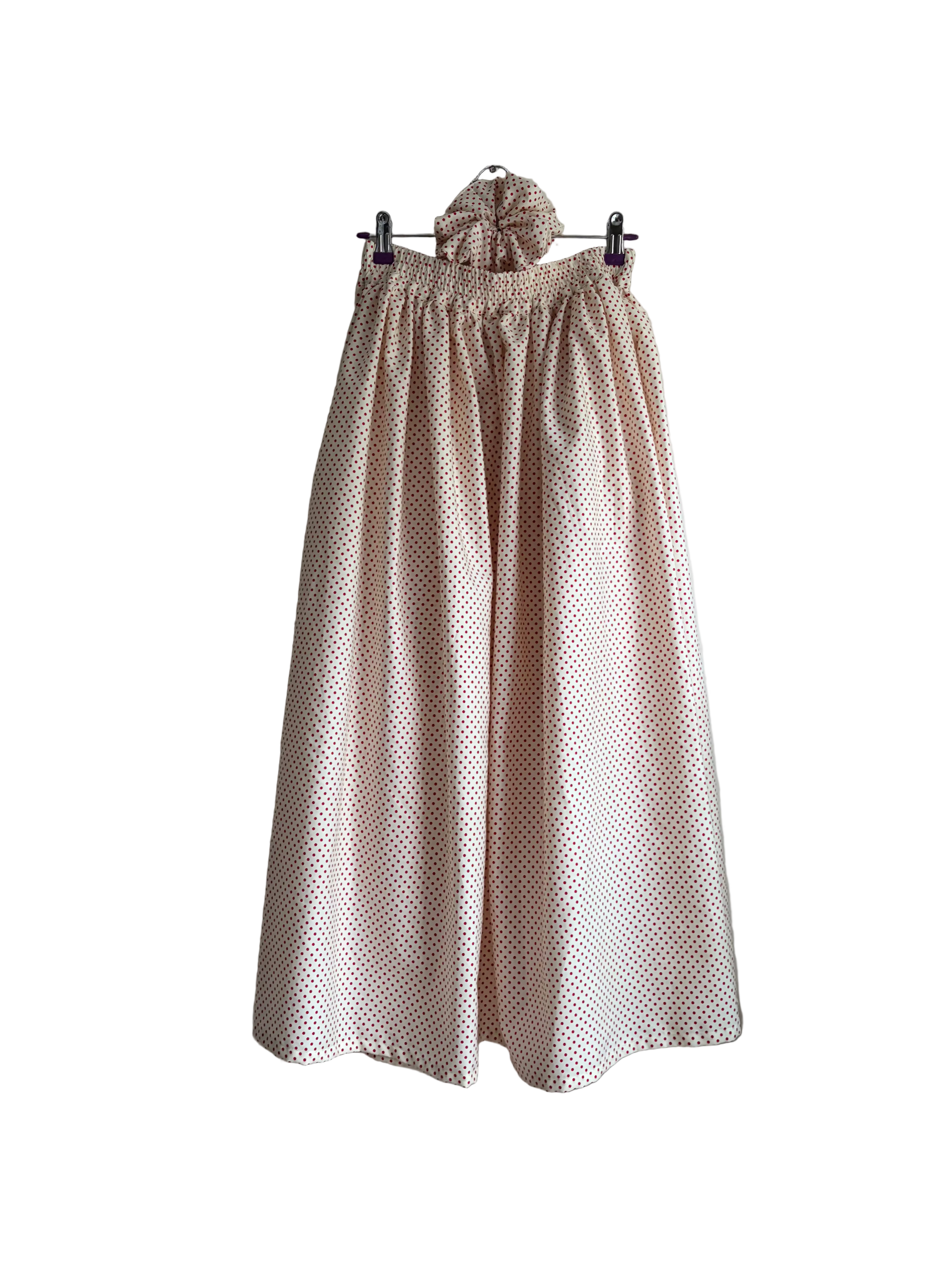 A light pink and white polka dot wide-leg skirt with an elastic waistband and matching scrunchie, hanging on a wall.
